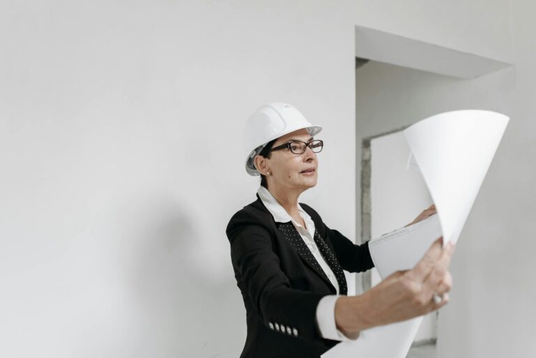 A professional female architect in a hard hat examines building plans on a construction site.