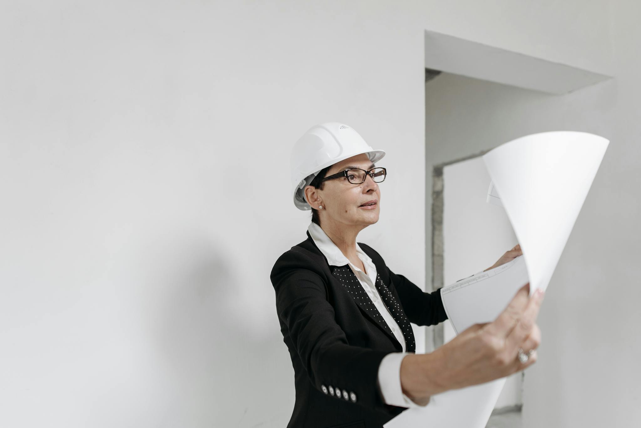 A professional female architect in a hard hat examines building plans on a construction site.