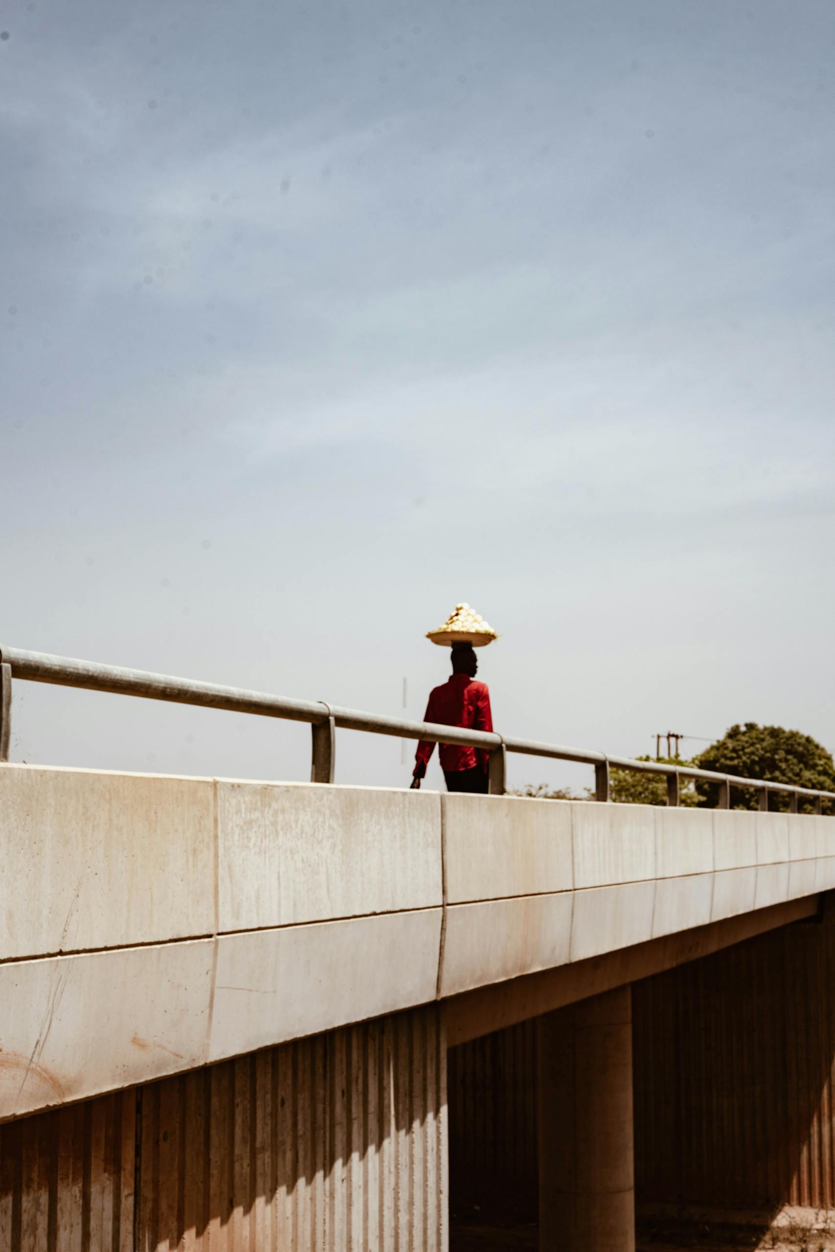 A person in traditional hat crossing a bridge under a clear blue sky in Abuja, Nigeria.